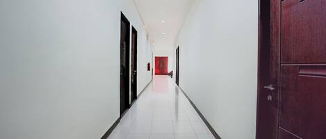 A corridor with white walls, a tiled floor, and a wooden door on the right.