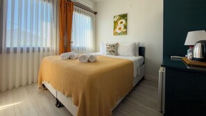 A hotel room with a bed, a painting, a desk with a kettle, and a window with curtains. - KAYA KORUĞU CUNDA (Ayvalik)