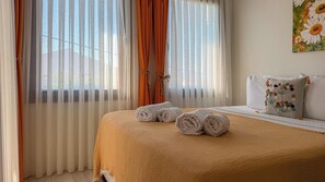 Una cama bien hecha con toallas enrolladas, una manta color beige y una almohada con diseño floral.