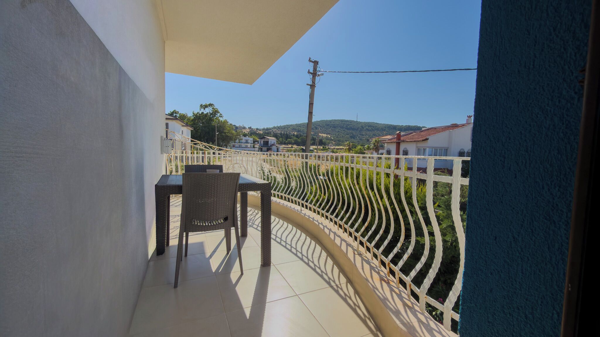 Un balcon avec une table et une chaise, une clôture blanche et une vue sur des maisons et des collines.