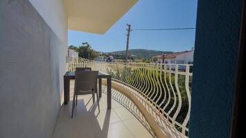 Un balcon avec une table et une chaise, une clôture blanche et une vue sur des maisons et des collines.