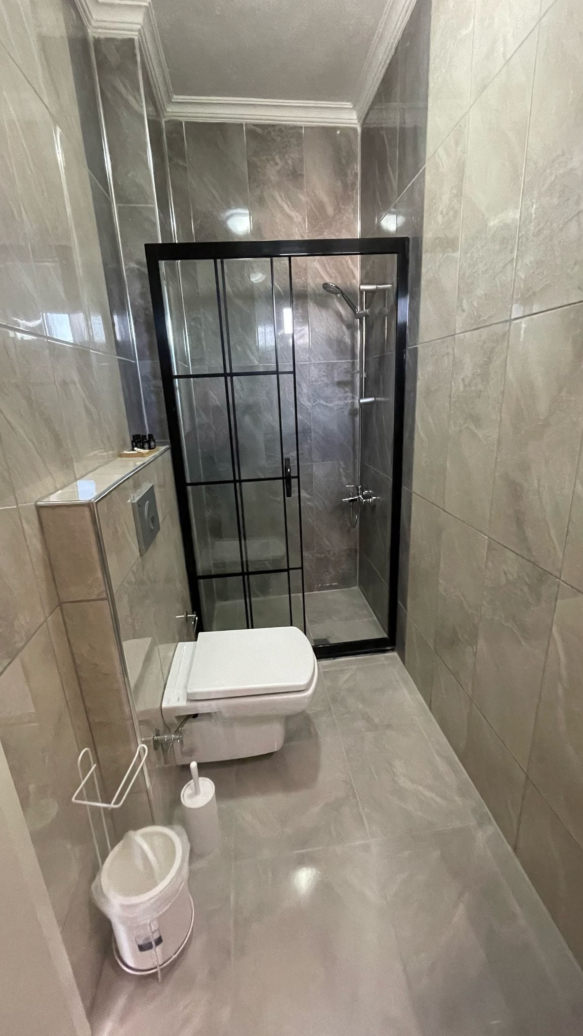 A modern bathroom with a glass-enclosed shower, a toilet, and a white bucket.