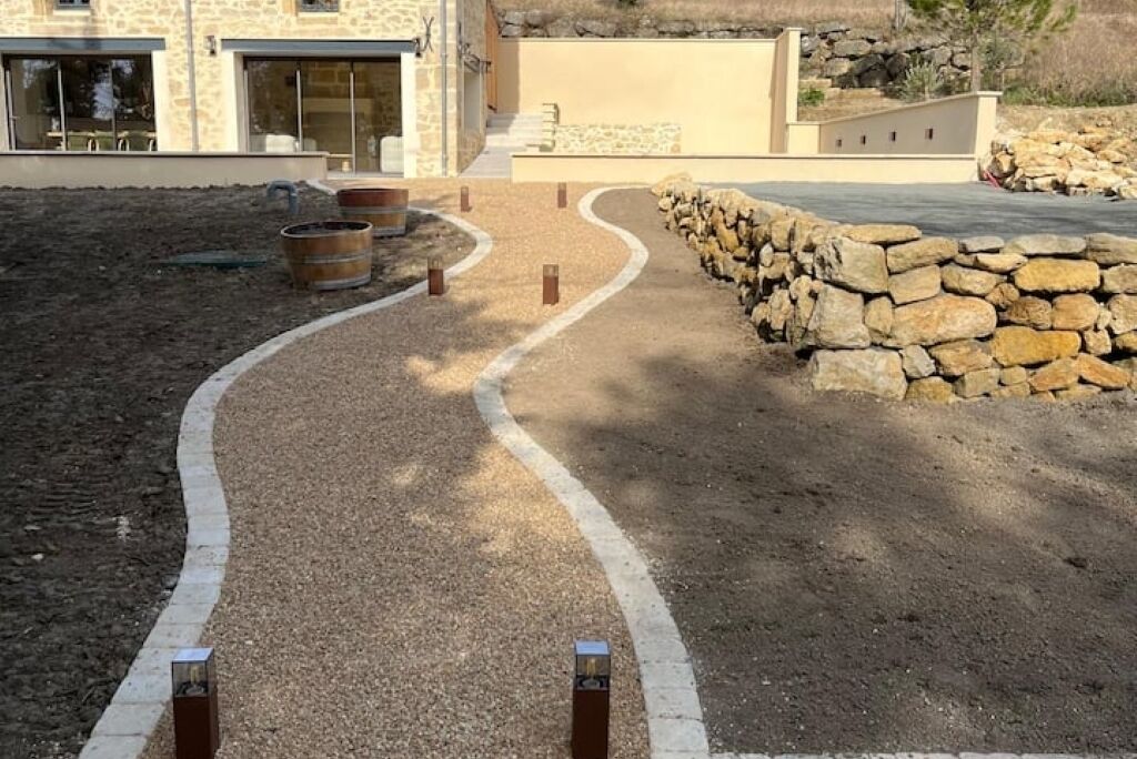 Un área ajardinada con un sendero de grava, un muro de piedra y mobiliario exterior.
