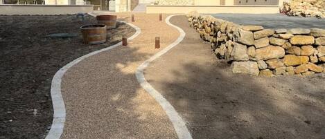 Un área ajardinada con un sendero de grava, un muro de piedra y mobiliario exterior.