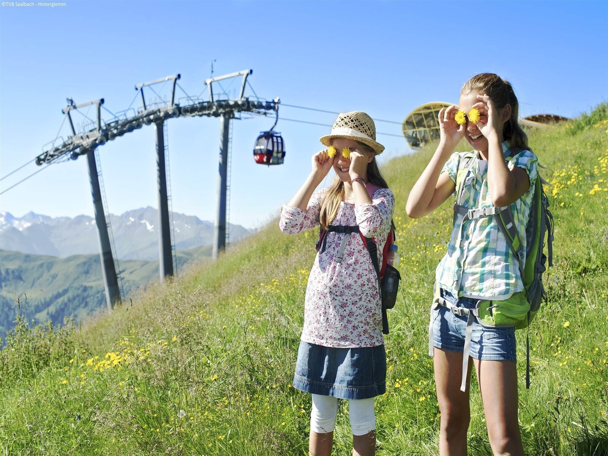 Two people standing on a grassy hill with a cable car in the background.