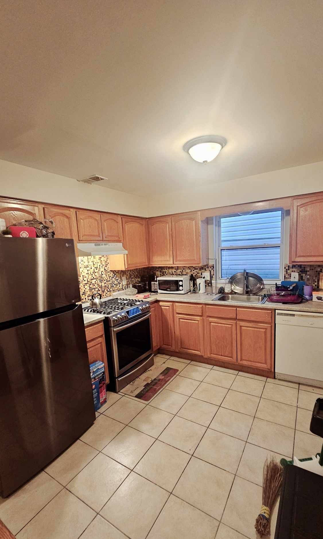 A kitchen with wooden cabinets, a stainless steel refrigerator, a microwave, and a stove.