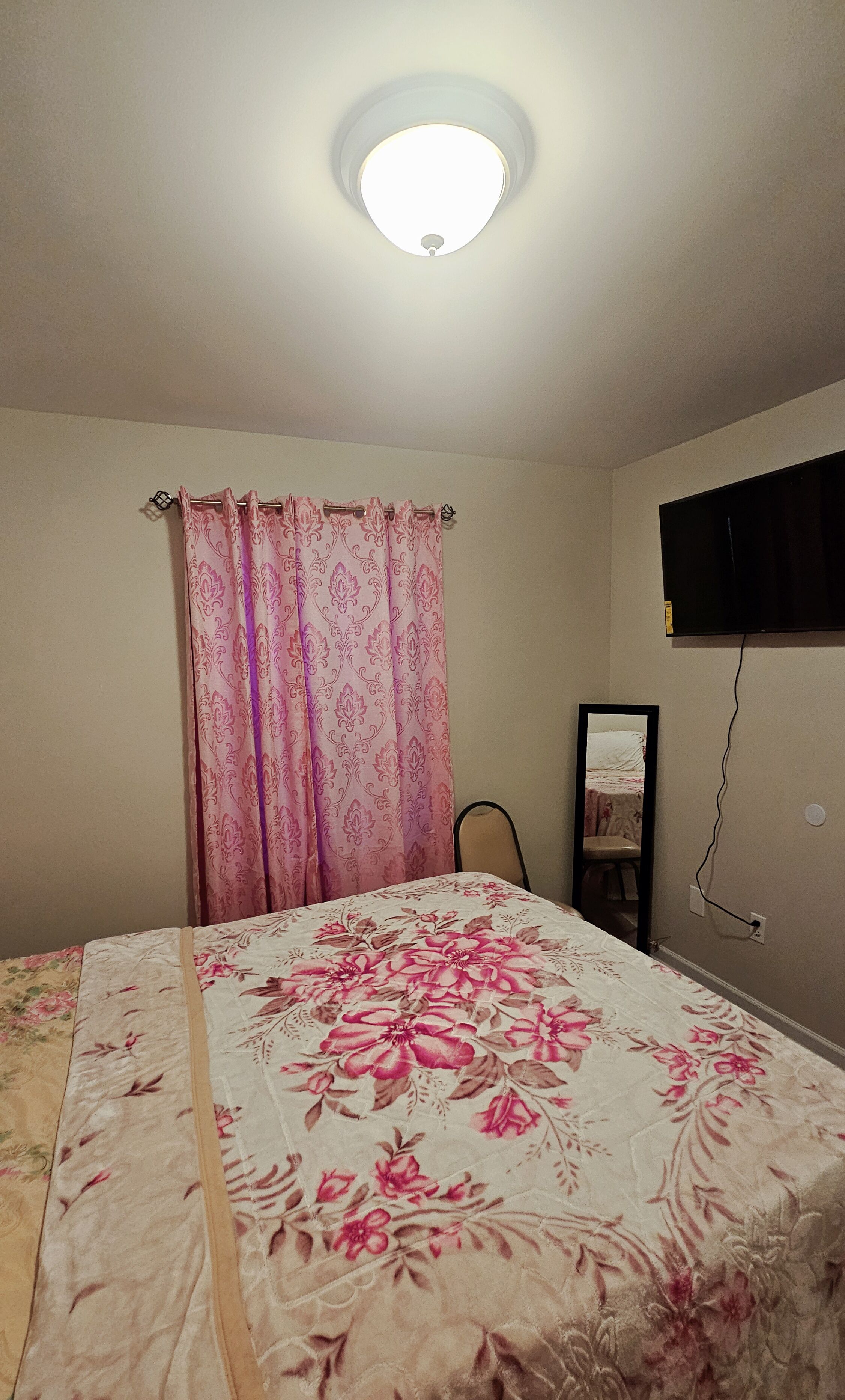 A bedroom with a bed, a curtain, a mirror, and a television mounted on the wall.