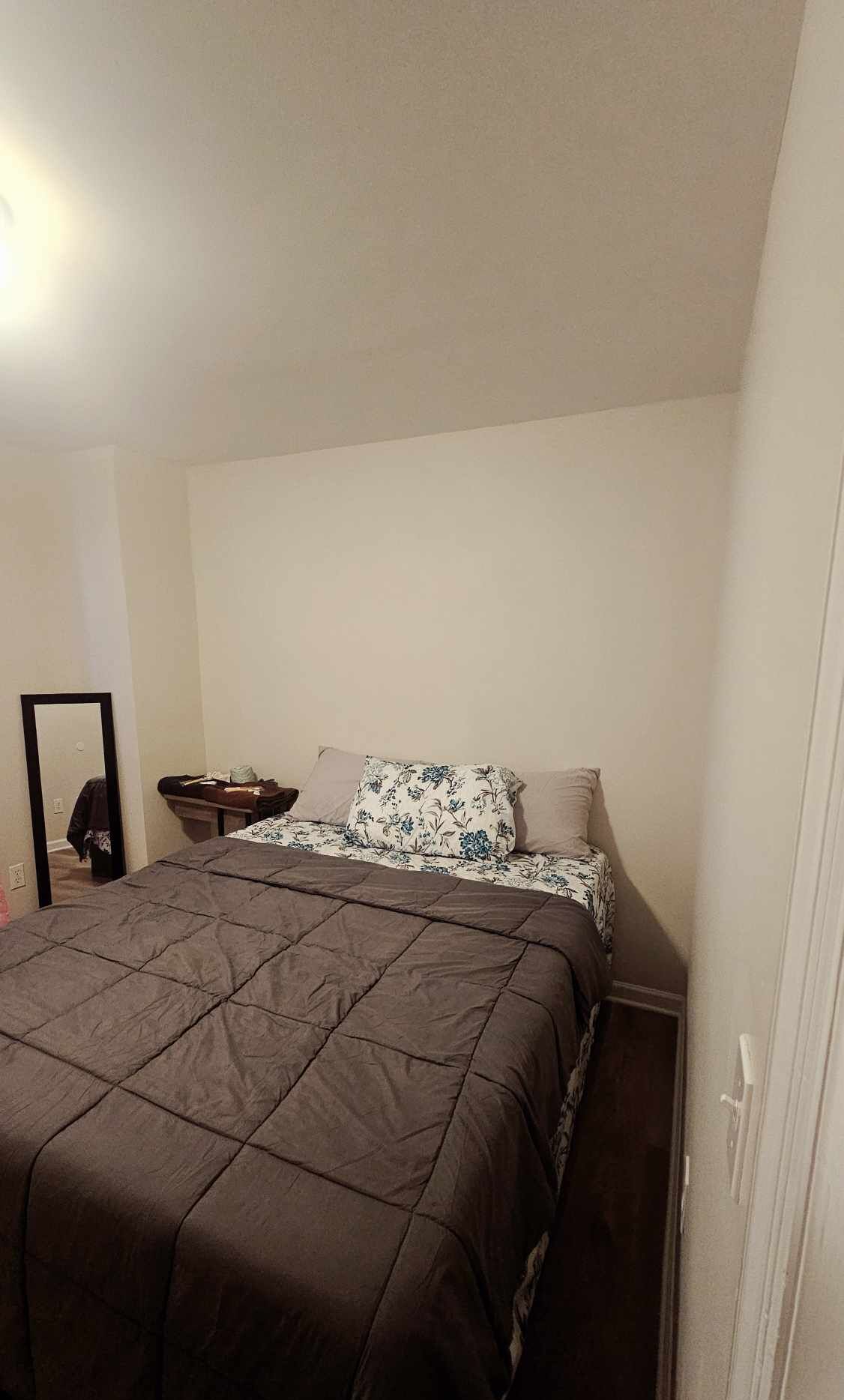 Une petite chambre simple, avec un lit simple, une table de chevet et un miroir.