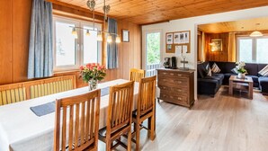 A wooden interior with a dining table, chairs, a sofa, and a dresser.
