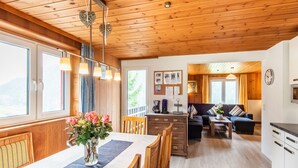 A wooden cabin interior with a dining area, kitchen, and living room.