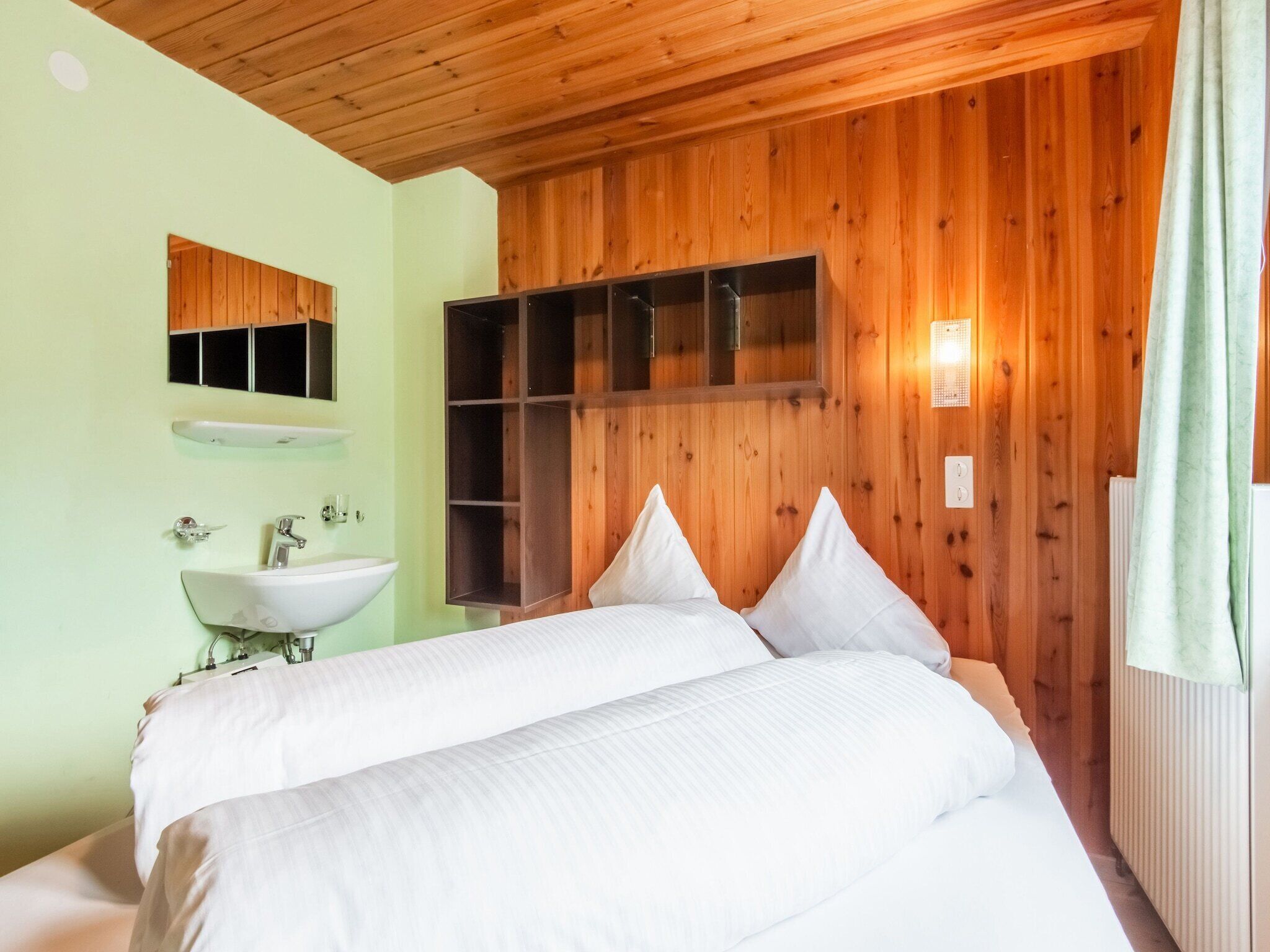 Une chambre avec un plafond en bois, un lit avec une literie blanche, une armoire en bois et une salle de bain avec un lavabo et un miroir.