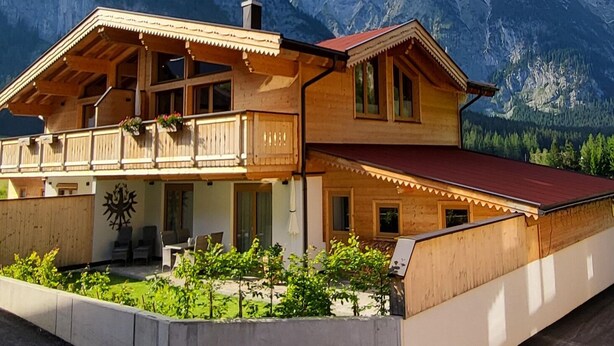 Een houten chalet met een balkon, een rood dak en een berg op de achtergrond.