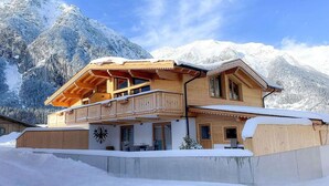Een houten chalet met balkon, gelegen tegen een besneeuwde berg.
