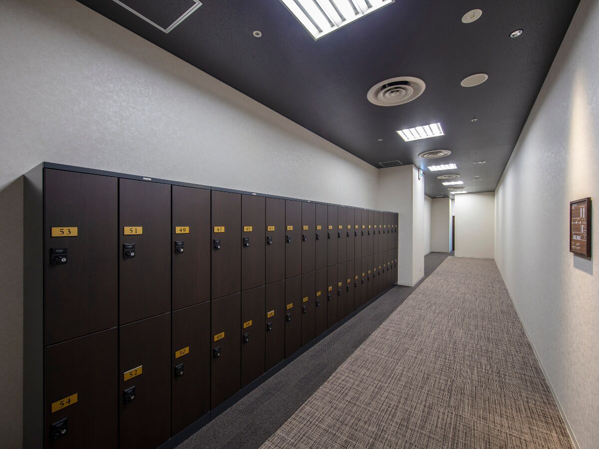 A long hallway with a row of dark brown lockers on the left, a carpeted floor, and recessed lighting on the ceiling.