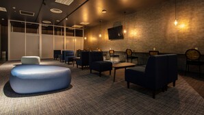A modern lounge area with seating, a large ottoman, and a TV mounted on the wall. - STATION INN THE URASHIMA (Onomichi)
