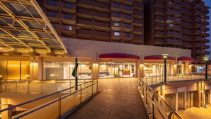 A hotel entrance with a glass facade, outdoor seating area, and a red awning. - STATION INN THE URASHIMA (Onomichi)