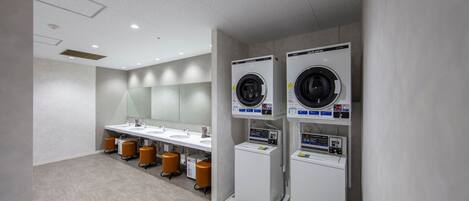 Un baño moderno con tres lavamanos, un espejo grande y dos lavadoras apiladas.