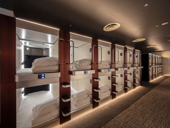 A row of bunk beds with built-in lighting, a carpeted floor, and a dark ceiling with recessed lighting. - STATION INN THE URASHIMA (Onomichi)