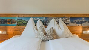A bedroom with a wooden headboard, white bedding, and multiple landscape paintings on the wall. - Apartment Brixen near Ski Lift (Brixen im Thale)