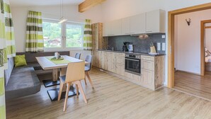 A modern kitchen with wooden cabinets, a dining area with a table and chairs, and a view of greenery outside. - Apartment Brixen near Ski Lift (Brixen im Thale)