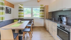 A modern kitchen with wooden cabinets, a built-in oven, and a dining area with a table and chairs. - Apartment Brixen near Ski Lift (Brixen im Thale)