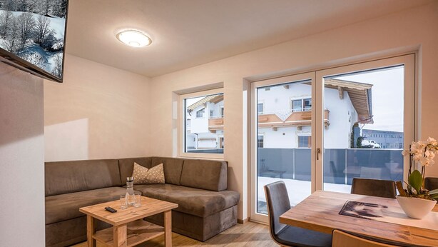 A modern living room with a brown sofa, a wooden coffee table, and a dining area with a table and chairs. - Apartment Brixen near Ski Lift (Brixen im Thale)