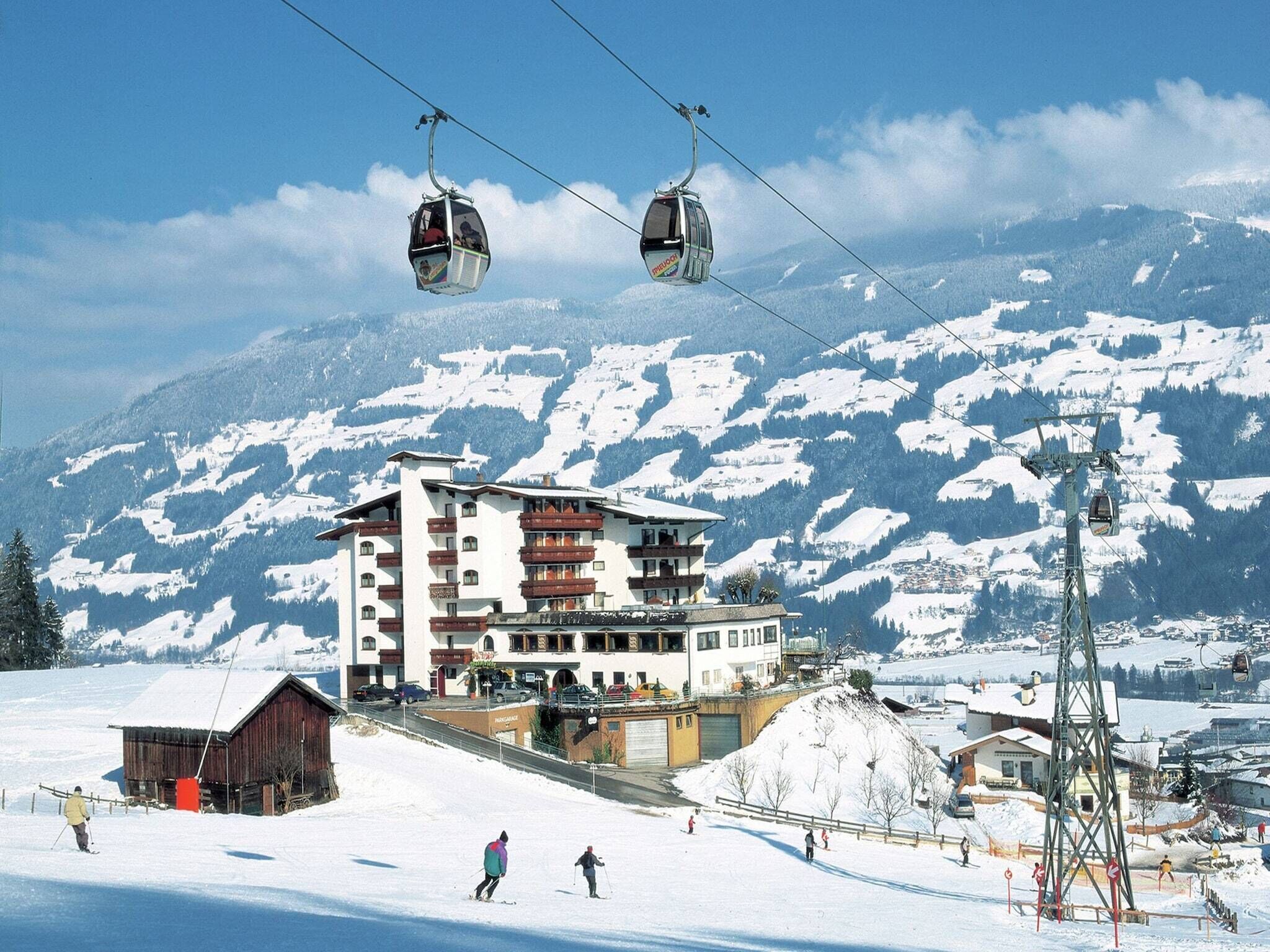 A ski resort with a multi-story building, ski lifts, and a snowy mountain backdrop.