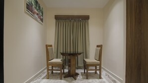 A dining area with a round table and two chairs, a beige rug, and a window with curtains. - Hotel Vista Suites (Tezpur)