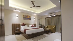 A modern hotel room with a large bed, a ceiling fan, recessed lighting, a flat-screen TV, a sofa, and a window with curtains. - Hotel Vista Suites (Tezpur)