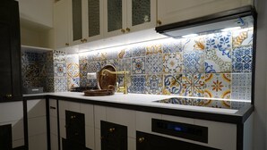 A kitchen with a white countertop, a sink, and a backsplash with colorful tiles. There are cabinets with gold handles and a clock on the wall. - Heart of Puglia - Design Apartment in Puglia with 2 bedrooms (Putignano)