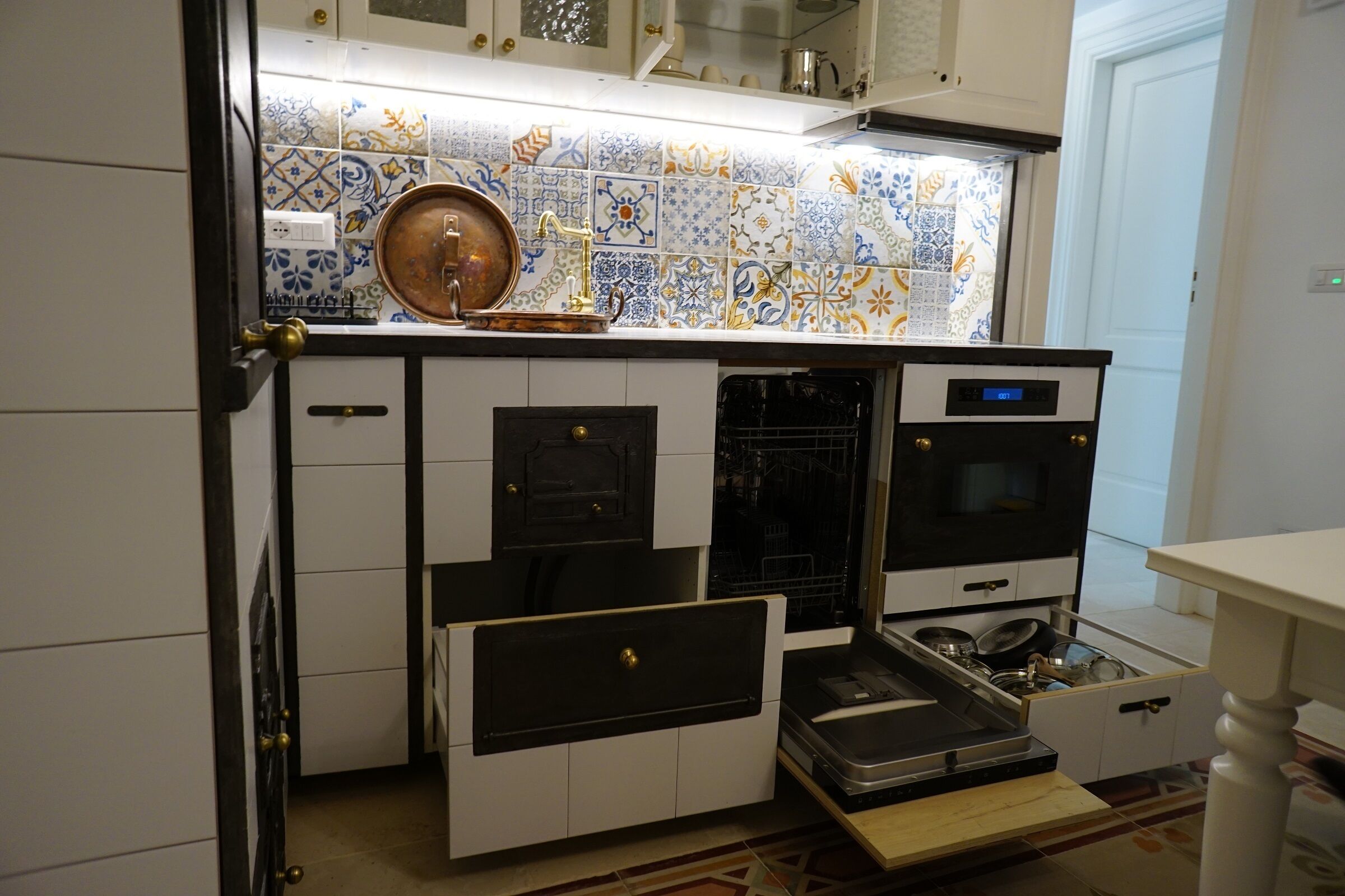 Una cocina con salpicadero de azulejos, una olla de cobre, una estufa y un lavavajillas.