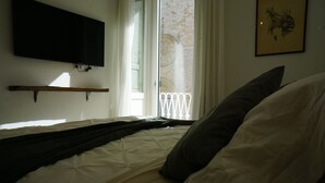 A bedroom with a bed, a mounted TV, a window with a view of a building, and a framed picture on the wall. - Heart of Puglia - Design Apartment in Puglia with 2 bedrooms (Putignano)