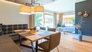 A modern living room with a wooden dining table, a sofa, and a large window with a view of greenery.