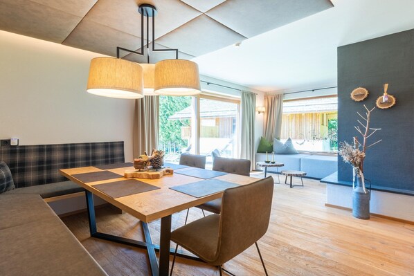 Uma sala de estar moderna com uma mesa de jantar de madeira, um sofá e uma janela grande com vista para o verde.