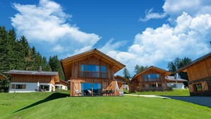 A wooden chalet-style building with a balcony, surrounded by a well-maintained lawn and trees.