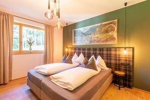Quarto com cama, janela com cortinas, pintura na parede e um pequeno banquinho.