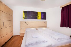 Ein Schlafzimmer mit einem hölzernen Kleiderschrank, einem Bett mit weißer Bettwäsche und einem farbenfrohen, abstrakten Gemälde an der Wand.