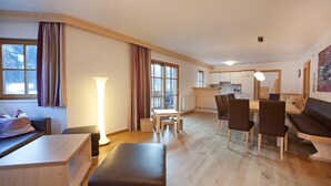 Un salon moderne avec un canapé, une table à manger et des chaises, une lampe et de grandes fenêtres avec des rideaux.