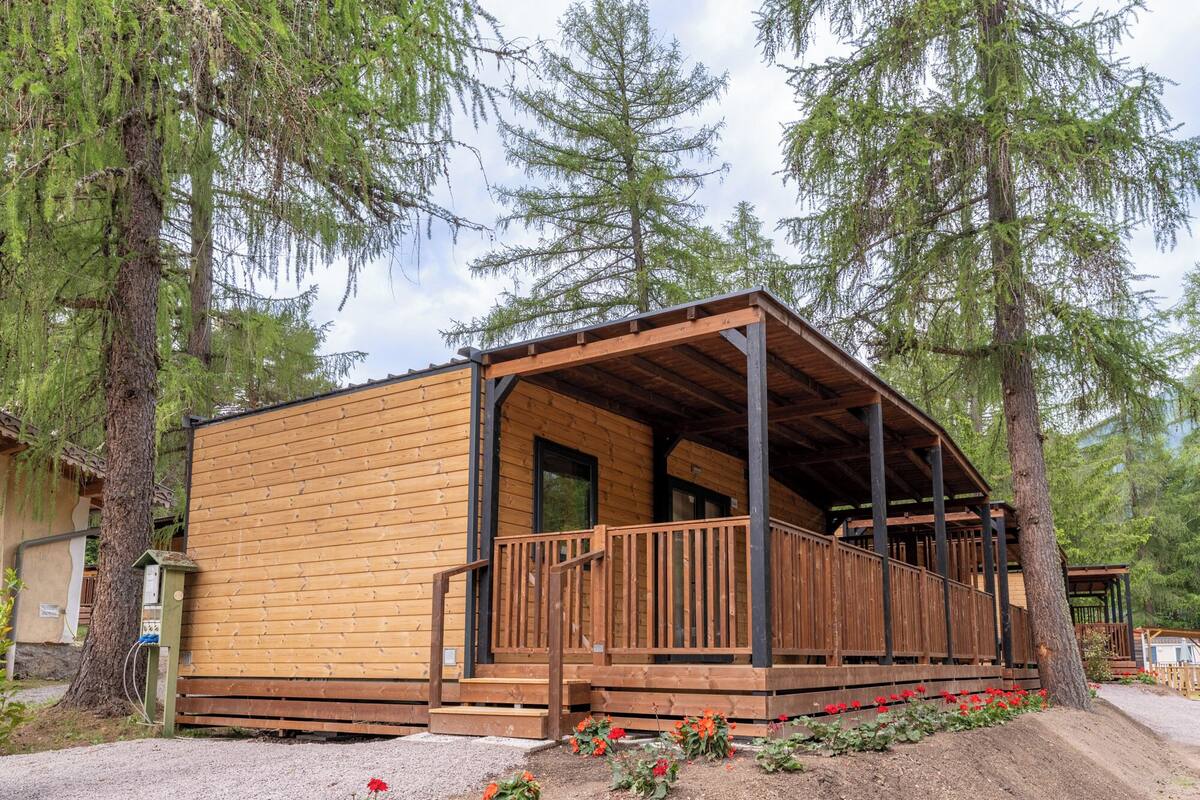 A wooden cabin with a porch, surrounded by trees.