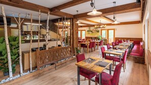 A restaurant with wooden beams, red upholstered chairs, and a long wooden table. - Club del Sole Val di Fiemme  (Bellamonte)