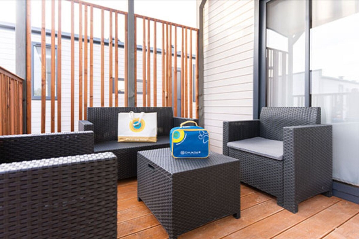 Un balcon avec des meubles en osier, un sac bleu et un sac blanc posés sur un plancher en bois.