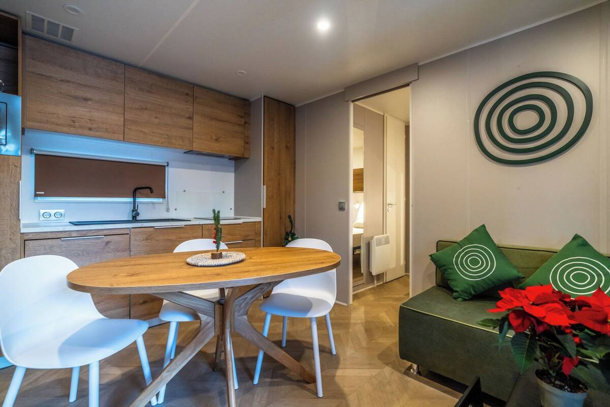 A modern kitchen with wooden cabinets, a dining table with chairs, and a living area with a sofa and decorative pillows.