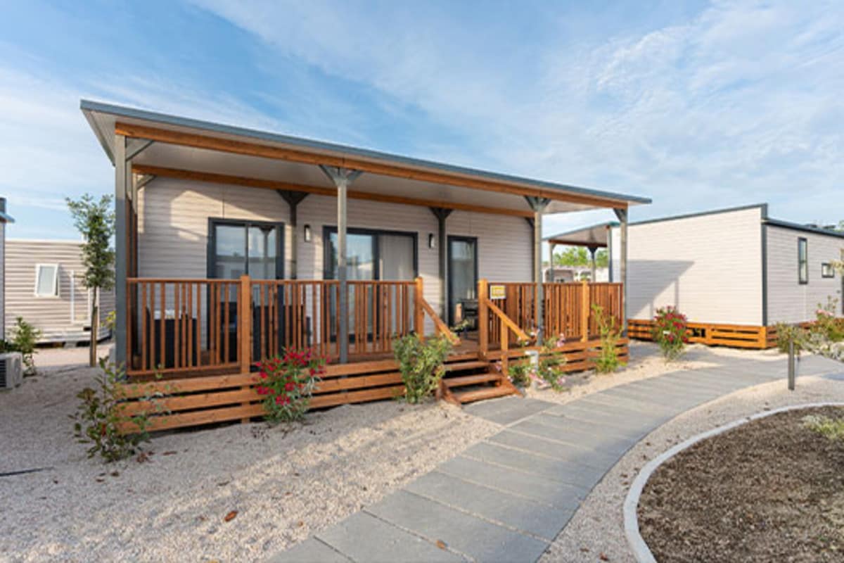 A modern mobile home with a wooden deck and a covered porch.