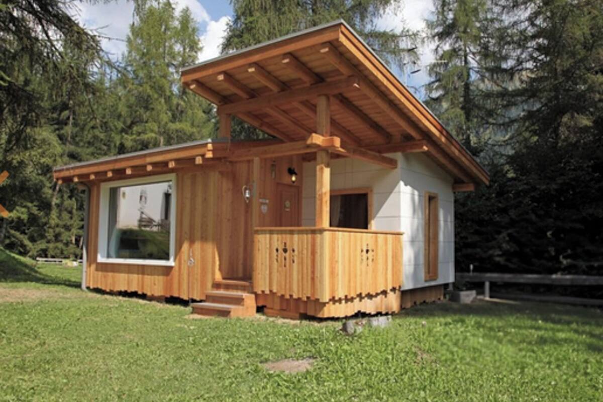 A wooden cabin with a large window, a porch, and a covered area.