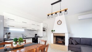 Eine moderne Küche mit weißen Schränken, einem Esstisch mit Stühlen, einem Kamin und einem grauen Sofa in einem Wohnbereich.