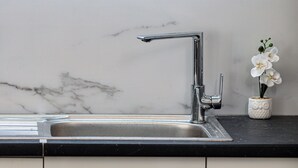 Eine Küche mit einem modernen Wasserhahn, einer Marmor-Spritzschutzwand und einer kleinen weißen Vase mit einer Orchidee.