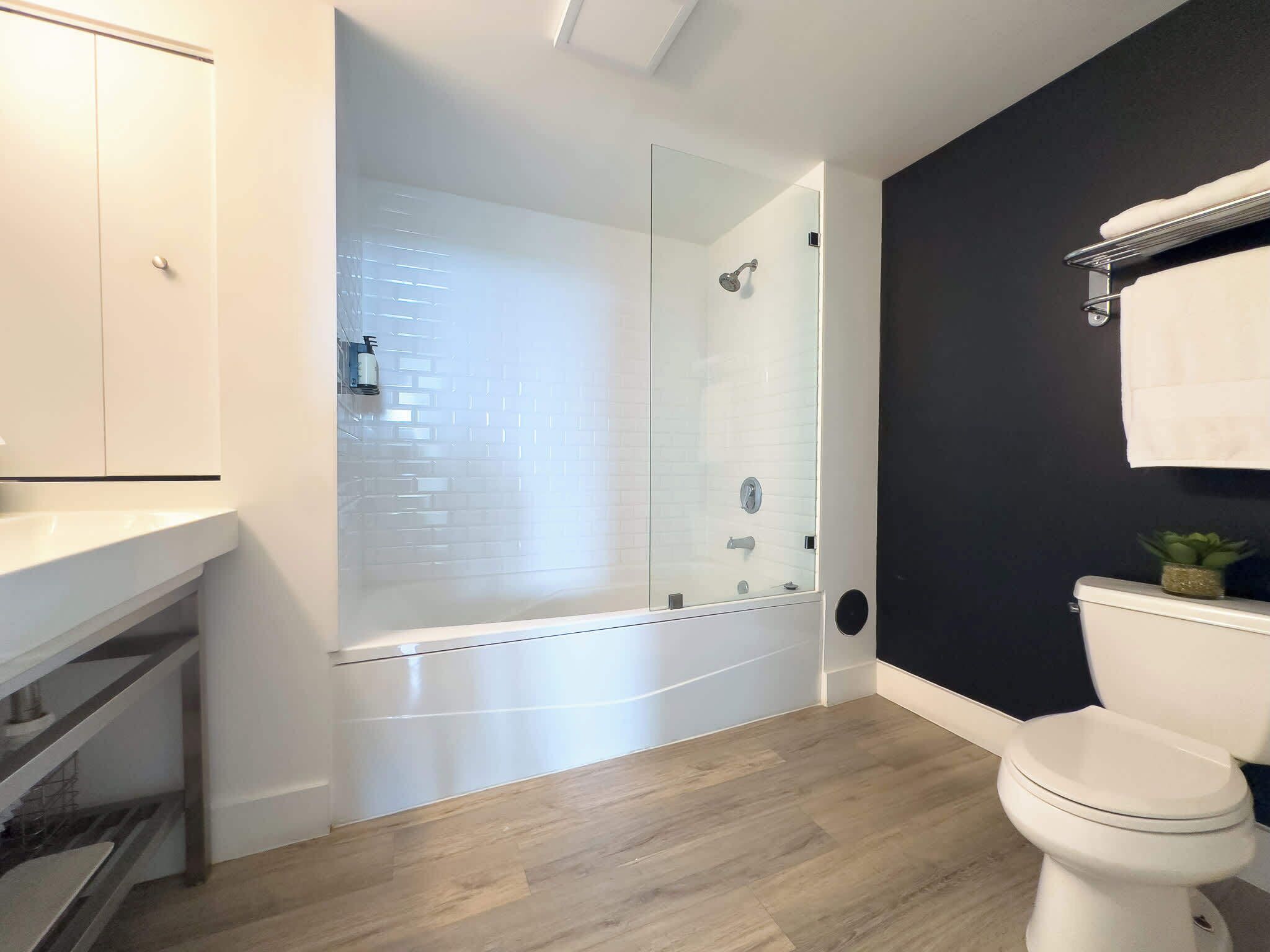 Ein modernes Badezimmer mit einer Glaskabine zur Dusche, einer weißen Toilette und einer dunkel gefärbten Wand.