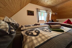Une chambre confortable avec un plafond en pente, un lit recouvert d’une literie à motifs, une fenêtre avec des rideaux et une armoire en bois.