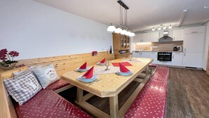 A compact kitchen with white cabinets, a wooden dining table set with red napkins, and a bench with red cushions. - Alpine House in Prebl near Klippitztörl Ski Area (Prebl)
