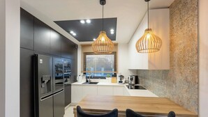 Une cuisine moderne avec des meubles de rangement noirs, une table à manger en bois et des luminaires suspendus.